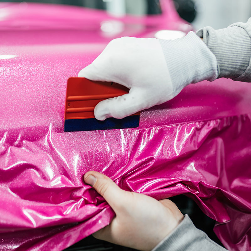 Gloved hands applying glossy pink wrap film with a squeegee