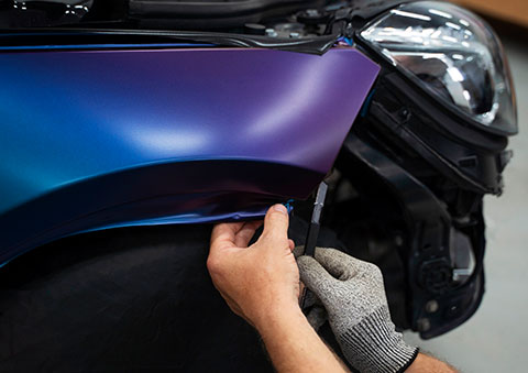 Hands stretching purple wrap film over a car fender