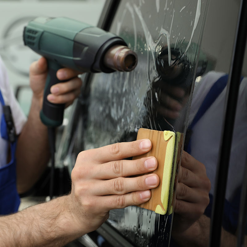 Installer using a heat gun and squeegee to shrink tint film on a car window